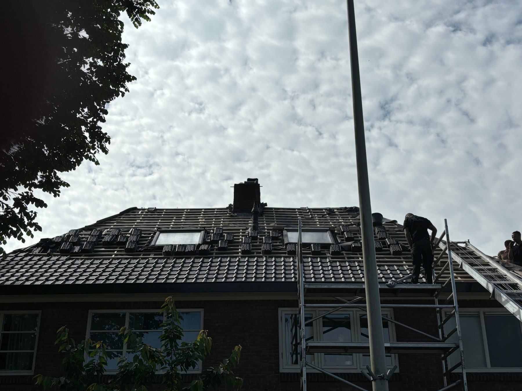 Dakdekkers aan het werk op een pannendak met steiger en ladder